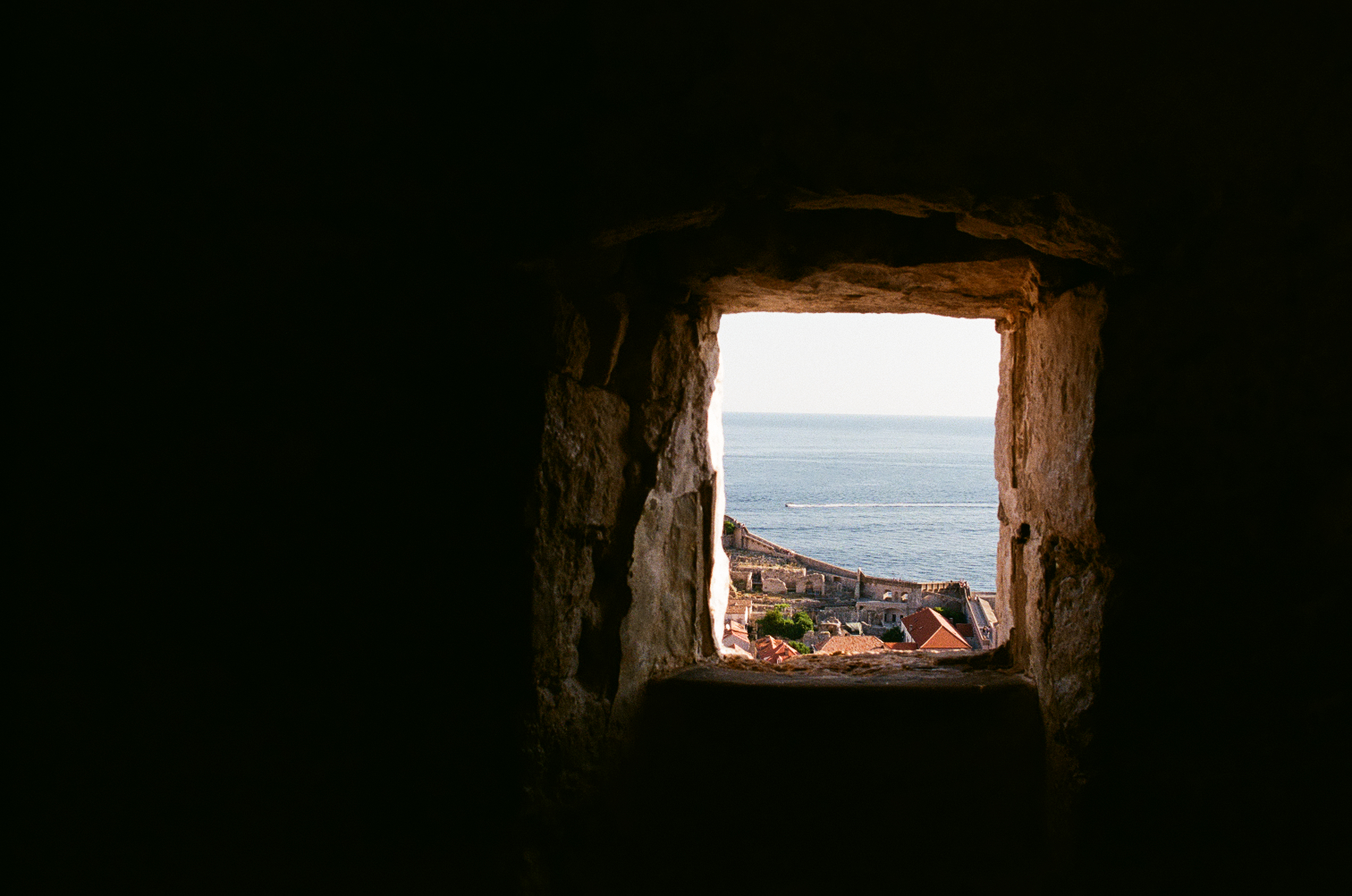 A stone window framing rooftops and the Adriatic Sea.